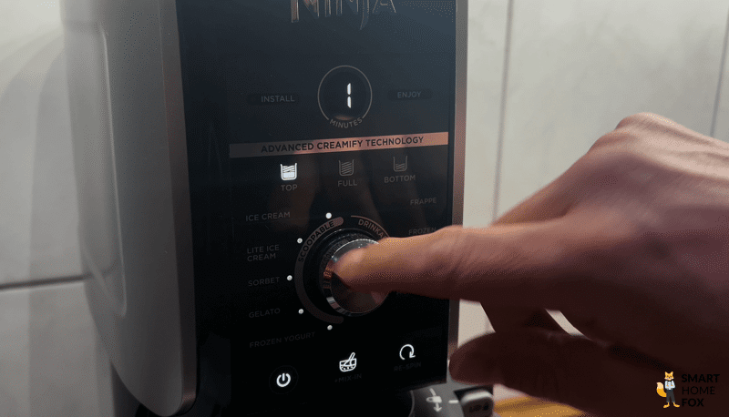 Ein Finger dreht das Auswahlrad der Ninja Creami Deluxe, um eines der neun Programme auszuwählen.